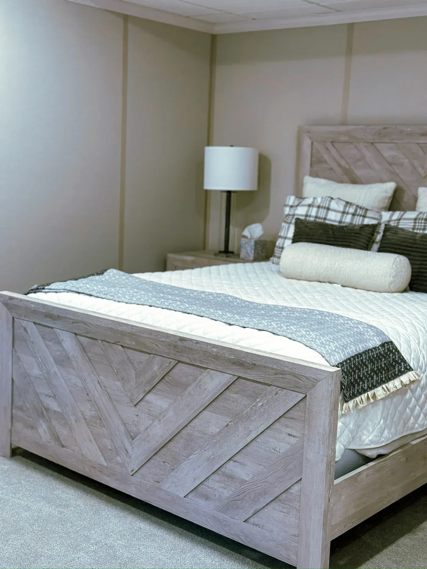 Cozy bedroom with a rustic wooden bed frame, adorned with plaid and textured pillows, a knitted throw, and a soft, inviting color palette.